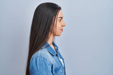 Mavi arka planda dikilen İspanyol kadın yan bakmak, rahat poz vermek doğal yüz ve kendine güvenen bir gülümseme.. 