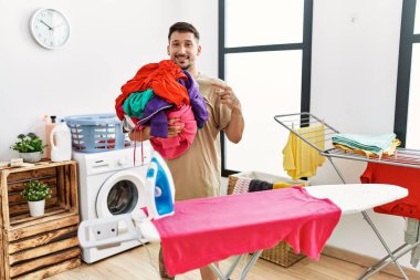 Young handsome man holding laundry ready to iron smiling happy pointing with hand and finger 