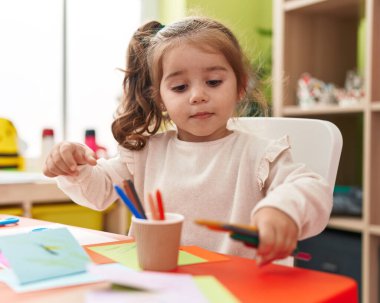 Anaokulunda masaya oturmuş kağıda resim çizen sevimli İspanyol kız öğrenci.