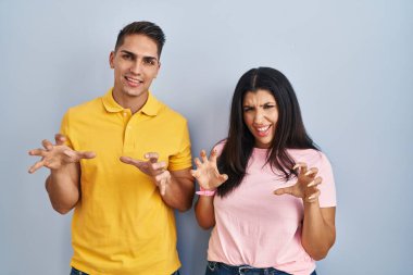 Soyutlanmış arka planda duran genç çift komik bir şekilde kedi gibi pençe hareketi yapıyor, agresif ve seksi bir ifade. 