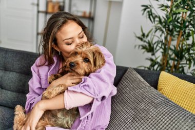 Evdeki kanepede oturan güzel İspanyol bir kadın köpeğe sarılıyor.