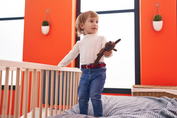 Adorable hispanic girl holding doll standing on bed at bedroom