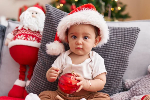 Adorable Hispanic Baby Holding Christmas Decoration Ball Sitting Sofa Home — Stock Photo, Image
