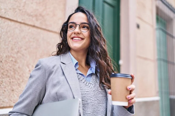 Young hispanic woman executive drinking coffee holding laptop at street