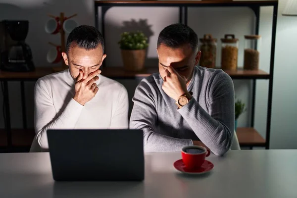 Homosexual couple using computer laptop tired rubbing nose and eyes feeling fatigue and headache. stress and frustration concept.