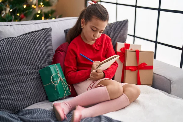 Adorable Hispanic Girl Writing Notebook Sitting Sofa Christmas Tree Home — Stock Photo, Image