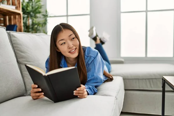 Young Chinese Girl Reading Book Lying Sofa Home — Stock Photo, Image