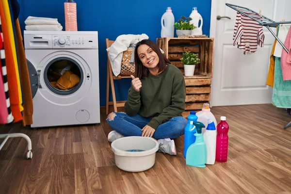 Young hispanic woman doing laundry washing by hand smiling happy and positive, thumb up doing excellent and approval sign