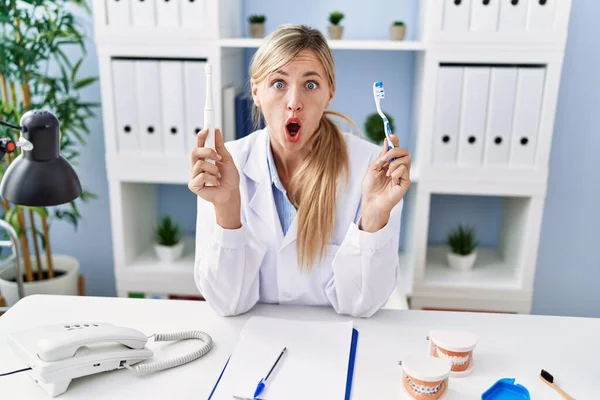 Beautiful Dentist Woman Holding Ordinary Toothbrush Electric Toothbrush Shock Face — Stock fotografie