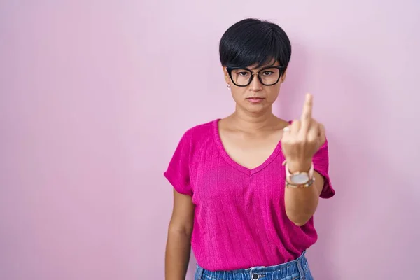 Young asian woman with short hair standing over pink background showing middle finger, impolite and rude fuck off expression