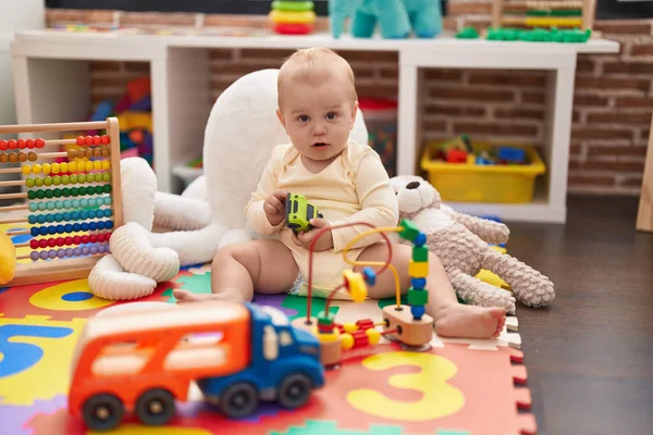 幼稚園の床に座っている車やトラックのおもちゃで遊ぶ愛らしい白人の赤ちゃん — ストック写真