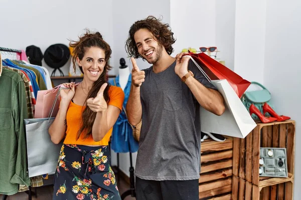 小売店で買い物袋を持っている若いヒスパニック系のカップルは 幸せで面白い顔をしたカメラに指を指しています 良いエネルギーと振動は — ストック写真