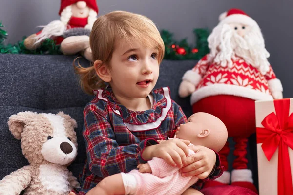 愛らしいですCaucasian女の子巨大赤ちゃん人形座っています上のソファによってクリスマス装飾で家 — ストック写真
