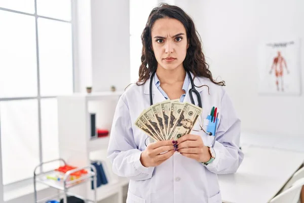 Young doctor woman holding money skeptic and nervous, frowning upset because of problem. negative person.