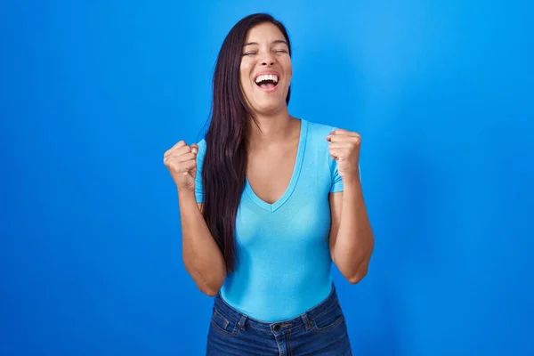 Молодая Латиноамериканка Стоящая Синем Фоне Взволнована Успехом Поднятыми Руками Закрытыми — стоковое фото