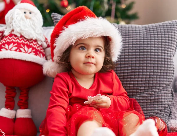 可爱的惊慌失措的女孩自信地坐在家里的圣诞树旁的沙发上 — 图库照片