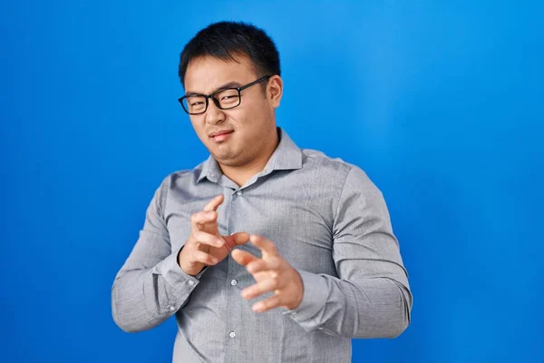 Young chinese man standing over blue background disgusted expression, displeased and fearful doing disgust face because aversion reaction. with hands raised