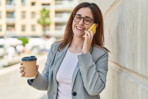 Genç iş kadını akıllı telefondan konuşuyor. Sokakta kahve içiyor.