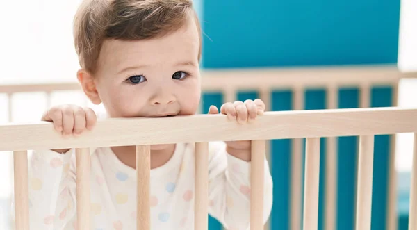 可爱的高加索婴儿站在摇篮上 咬着卧室里的木制栏杆 — 图库照片