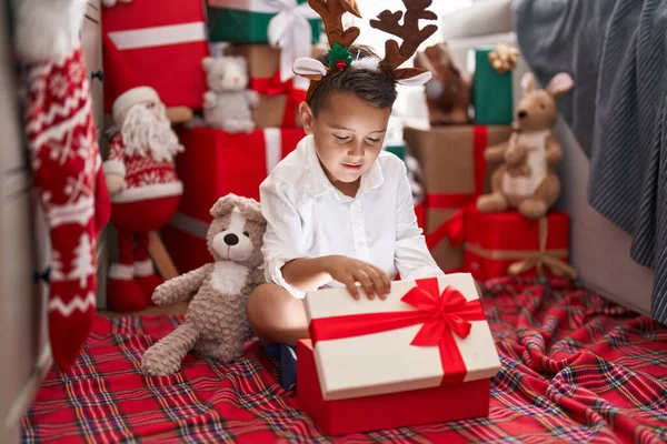 Uroczy Latynoski Maluch Rozpakowujący Świąteczny Prezent Siedząc Podłodze Domu — Zdjęcie stockowe