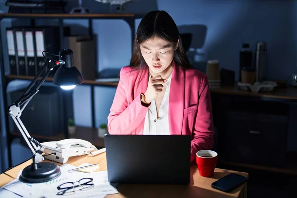 Chinese young woman working at the office at night feeling unwell and coughing as symptom for cold or bronchitis. health care concept.
