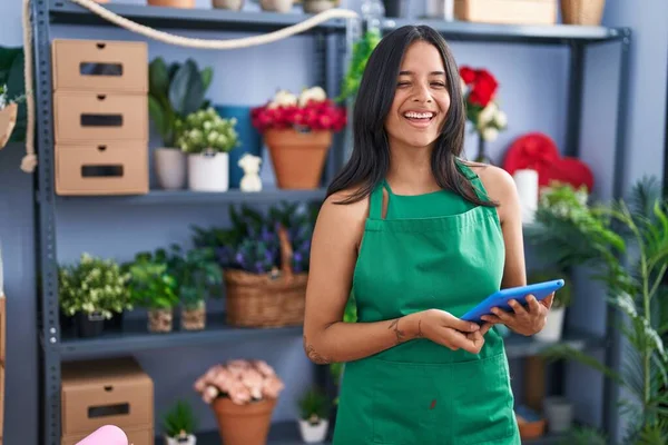 Brunette woman working at florist shop holding tablet winking looking at the camera with sexy expression, cheerful and happy face.