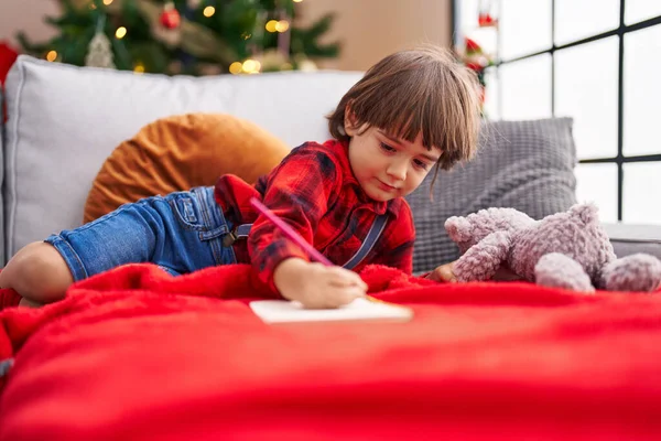 Criança Adorável Escrevendo Caderno Deitado Sofá Pela Árvore Natal Casa — Fotografia de Stock