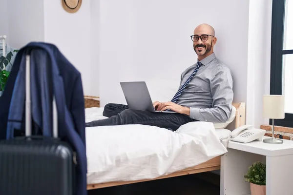 Young hispanic man business worker using laptop sitting on bed at hotel room