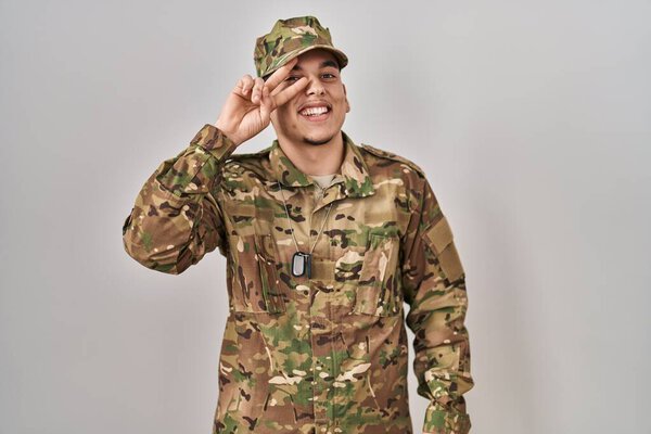 Young arab man wearing camouflage army uniform doing peace symbol with fingers over face, smiling cheerful showing victory 