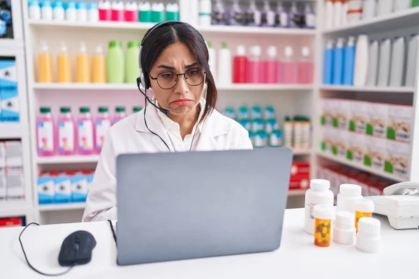 Young arab woman working at pharmacy drugstore using laptop depressed and worry for distress, crying angry and afraid. sad expression.