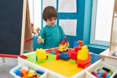 Adorable toddler playing with construction blocks standing at kindergarten