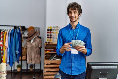 Young hispanic man counting dollars working at clothing store