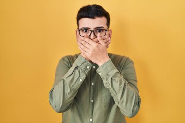 Non binary person standing over yellow background shocked covering mouth with hands for mistake. secret concept. 