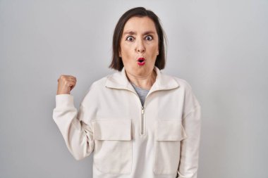 Orta yaşlı, ispanyol bir kadın, izole edilmiş arka planda durup, elleri yana dönük, ağzı açık, şaşkın bir ifadeyle şaşırdı.. 