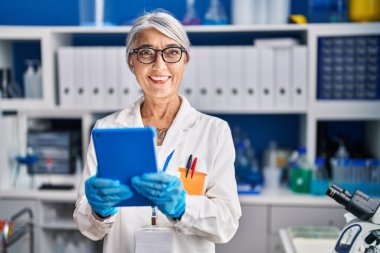 Orta yaşlı, gri saçlı kadın bilim adamı. Laboratuvarda çalışan dokunmatik ped kullanıyor.