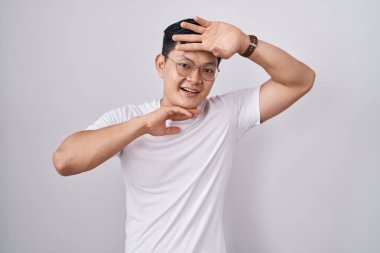 Young asian man standing over white background smiling cheerful playing peek a boo with hands showing face. surprised and exited 