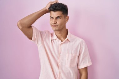 Pembe arka planda duran İspanyol genç adamın kafası karışmış ve soru sormayı merak ediyor. Şüpheyle kararsız, kafa kafaya düşünerek. Düşünceli kavram. 