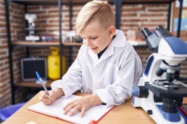 Sevimli çocuk, gülümseyen, kendine güvenen sınıftaki not defterine yazan öğrenci.