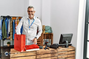 Orta yaşlı, gri saçlı bir dükkan asistanı giyim mağazasından alışveriş yapmaya hazırlanıyor.