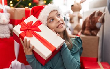 Sevimli İspanyol kız elinde hediyeyle evde Noel ağacının yanında oturuyor.