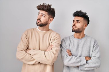Young homosexual couple standing over white background looking to the side with arms crossed convinced and confident 