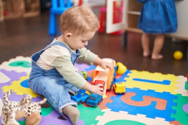 Adorable toddler playing with car toy sitting on floor at kindergarten