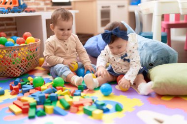Anaokulunda yerde oturmuş hayalarıyla oynayan iki çocuk.