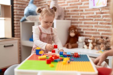 Sevimli beyaz kız anaokulunda duran inşaat bloklarıyla oynuyor.