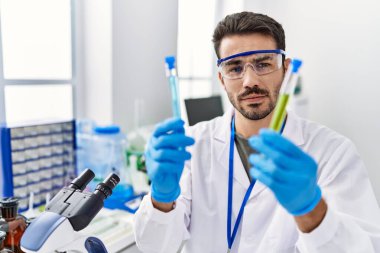 Laboratuvarda test tüpleri tutan bilim adamı üniforması giyen İspanyol bir genç.