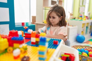 Anaokulundaki masada oturan, inşaat bloklarıyla oynayan sevimli İspanyol kız.