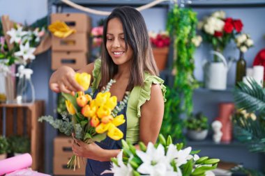 Young hispanic woman florist holding bouquet of flowers at florist store