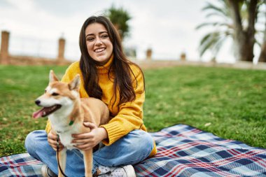 Güzel genç bir kadın parkta mutlu Shiba Inu köpeğine sarılıyor.