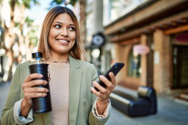 Sokakta akıllı telefon kullanan, kendine güvenen genç Latin bir kadın.