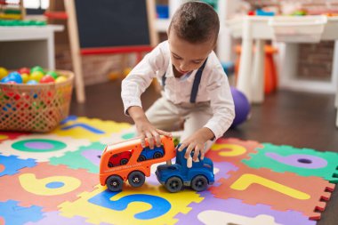 Adorable toddler playing with truck toy sitting on floor at kindergarten